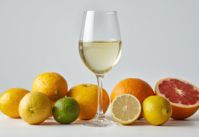 Copa de vino blanco elegante rodeada de cítricos frescos_ limones amarillos, limas verdes y toronjas